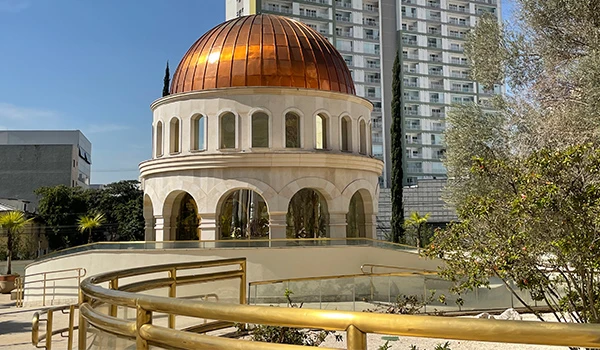 Imagem do prédio Espaço Sagrado com detalhes arquitetônicos marcantes, destacando uma cúpula dourada e janelas amplas, rodeado por vegetação e edifícios modernos, durante a visita guiada ao Templo de Salomão.
