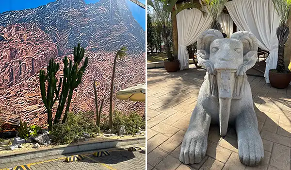 Imagem de um cenário ao ar livre com um mural de montanhas e cactos, ao lado de uma escultura de leão em um ambiente de descanso, durante a visita guiada ao Templo de Salomão.