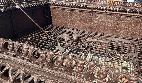 Imagem de um ornamento de ferro fundido, com detalhes em relevo e uma grade, ideal para apreciação da arte e arquitetura.