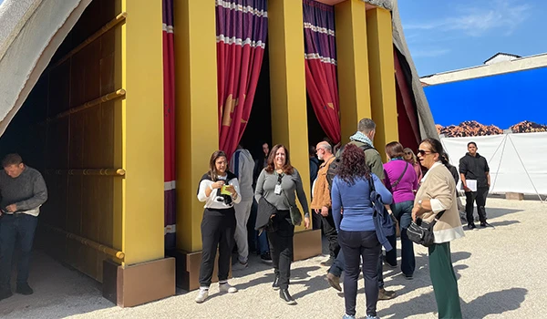 Grupo de pessoas na entrada de um grande espaço decorado, com cortinas vermelhas e paredes amarelas, em um evento ao ar livre, durante a visita guiada ao Templo de Salomão.