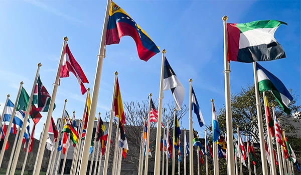 Bandeiras de vários países sob um céu azul claro, representando diversidade cultural e nações unidas em um espaço ao ar livre na entrada do Templo de Salomão.