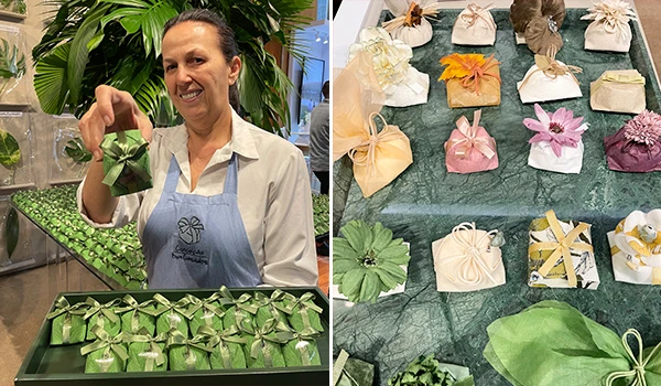 A imagem mostra uma mulher segurando um bem-casado, rodeada por vários outros embrulhos elegantes em uma mesa. Ela está em um ambiente com plantas, enfatizando a criatividade em um dos eventos para casamento em São Paulo.