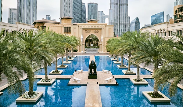 Vista deslumbrante do Hotel Palácio Downtown na água, cercado por palmeiras e edifícios altos, refletindo a arquitetura moderna de Dubai.