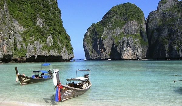 Praia deslumbrante com barcos de madeira em águas cristalinas, cercada por imensas formações rochosas verdes. Um verdadeiro paraíso tropical.