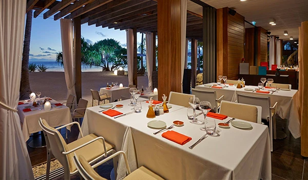 Ambiente sofisticado de restaurante com mesas elegantemente arrumadas e vista para o mar, ideal para jantares românticos e especiais.