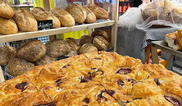 Pães artesanais e uma focaccia com azeitonas em uma padaria, exibindo variedade de pães tradicionais e uma deliciosa focaccia em primeiro plano. Mercado de Santo Amaro restaurantes.