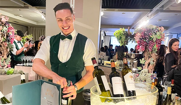 Um barman sorridente está servindo vinho em um evento elegante repleto de convidados. A imagem destaca a atmosfera festiva e luxuosa em um dos Eventos sobre casamento em São Paulo.