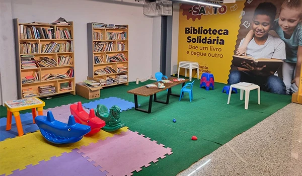 Espaço de leitura infantil em biblioteca solidária com livros, brinquedos e área de diversão, promovendo incentivo à leitura e ao acesso ao conhecimento.