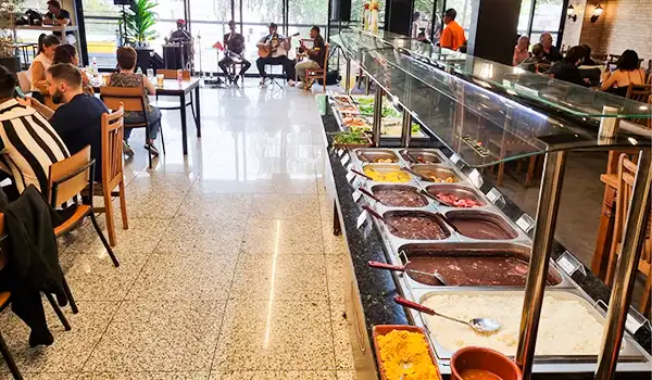 Ambiente de restaurante com buffet de sobremesas variado e clientes saboreando suas refeições, iluminado naturalmente. Mercado de Santo Amaro restaurante.