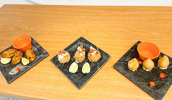 Três pratos de petiscos sofisticados de comida japonesa com diferentes molhos e acompanhamentos, dispostos em tábuas de pedra sobre uma mesa de madeira. Mercado de Santo Amaro restaurantes.