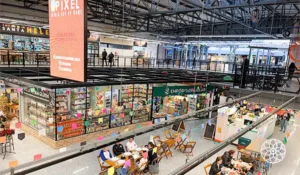 Imagem do Mercado de Santo Amaro com várias lojas abertas, pessoas sentadas em mesas e uma área com decoração colorida, promovendo comércio e lazer no centro comercial.