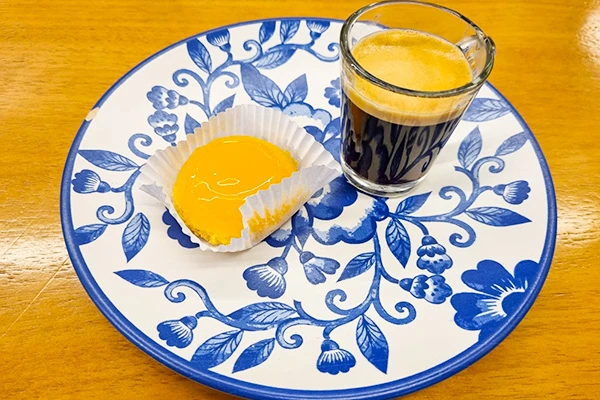 Quindim com café expresso servido em um prato decorado com motivos florais azuis. Uma combinação deliciosa para o café da manhã ou lanche. Mercado de Santo Amaro restaurantes.