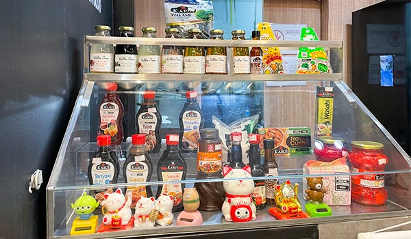 Variedade de molhos e condimentos para culinária exibidos em uma geladeira transparente, incluindo produtos tradicionais e itens decorativos na frente. Ideal para quem busca ingredientes para cozinha japonesa ou asiática.