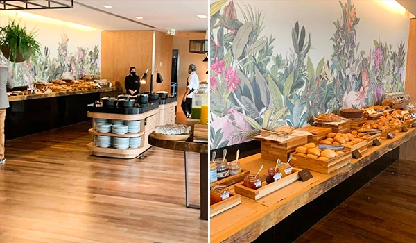 Ambiente de buffet com variedade de pães e doces, decoração tropical ao fundo, perfeito para um café da manhã sofisticado.