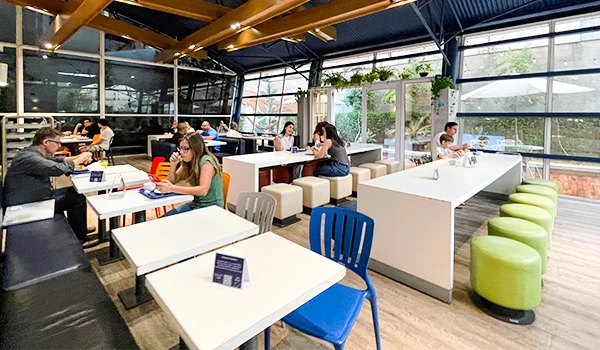 Ambiente de café da manhã moderno com mesas e cadeiras coloridas, clientes interagindo em um espaço iluminado e aconchegante.