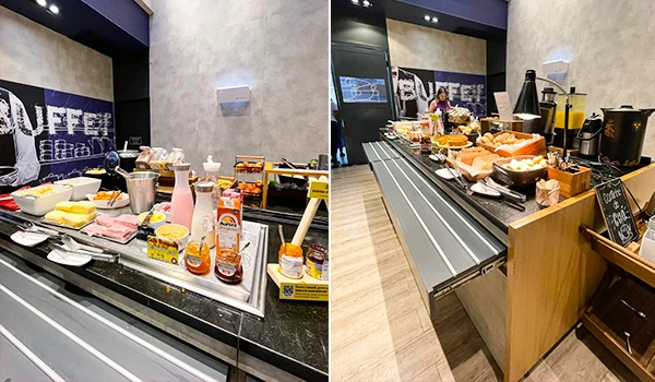 Buffet variado com opções de café da manhã, incluindo pães, frios, bebidas e itens de confeitaria em ambiente moderno.