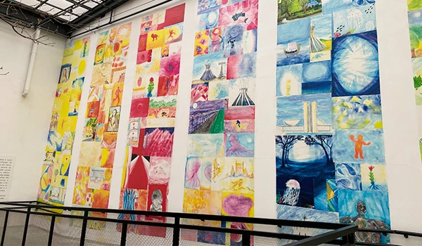 Exposição de obras de arte infantil com pinturas coloridas e variadas, apresentadas em uma parede de galeria, promovendo criatividade e expressão artística.
