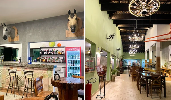 Restaurante rústico com balcão de bar, bebidas expostas em geladeira e prateleiras, mesas e cadeiras de madeira, luminárias decorativas feitas com rodas de carroça e cabeças de cavalos empalhadas nas paredes.