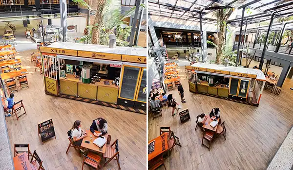 Imagem de um quiosque de comida fast food na área de um shopping ou centro comercial, com mesas e cadeiras ao redor, onde algumas pessoas estão fazendo pedidos e consumindo. Mercado de Santo Amaro restaurantes.