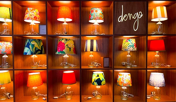 Exposição de abajures coloridos na loja Dengo, com diferentes estilos e padrões, iluminando o ambiente de forma vibrante e acolhedora.
