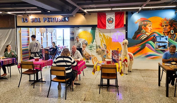 Interior de restaurante peruano com decoração colorida, mesas com toalhas vermelhas e um mural artístico que celebra a cultura peruana, com informações sobre o Sal Peruano.
