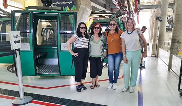 Deusa Rodrigues e outras três blogueiras de viagem sorridentes, posando na estação dos Bondinhos de Aparecida.