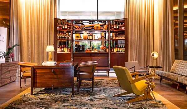 Foto de uma área do Hotel Rosewood São Paulo, com mesa, poltronas, sofá e estante, em ambiente de luxo, um dos hotéis mais caros de SP.