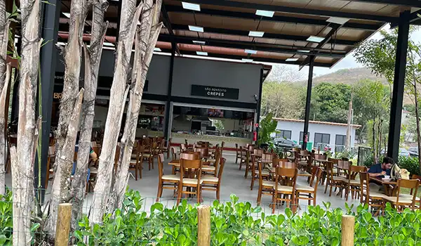 Espaço gastronômico ao ar livre com mesas de jantar sob teto, cercado por árvores e vegetação, ideal para refeições ao ar livre.