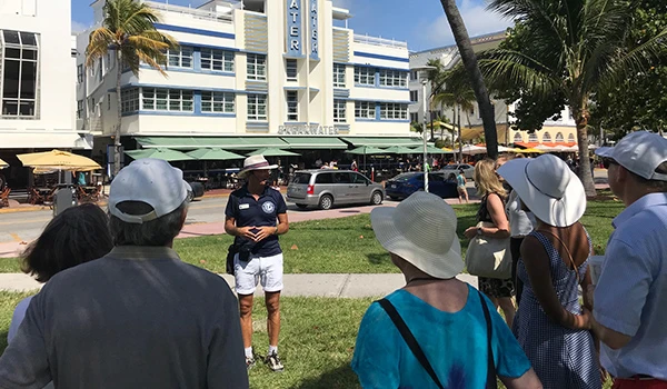 Grupo de turistas em South Beach, Miami, participando de uma visita guiada em um dia ensolarado, com destaque para o guia turístico e o ambiente vibrante.