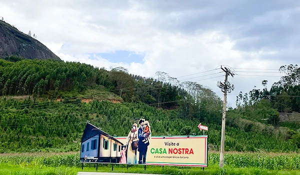 Placa publicitária para da Casa Nostra, destacando um convite para visitar e experimentar a culinária italiana em um cenário natural. Rota das Montanhas Capixabas.