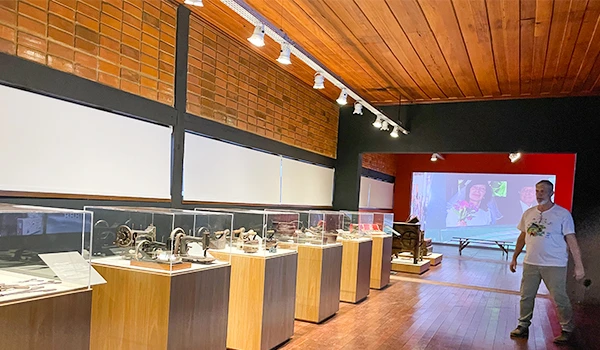Interior da Casa Nostra com exposições de máquinas antigas em vitrines de vidro. Um homem está andando pelo espaço, iluminado por luzes no teto.