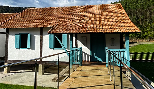 Uma casa com telhado de cerâmica laranja e janelas azuis em um ambiente natural, representando a vida dos imigrantes italianos na Casa Nostra, Rota das Montanhas Capixabas.