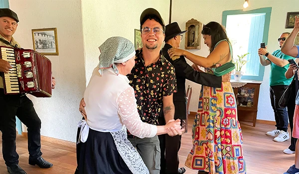 Interação de atores pessoas dançando em um ambiente decorado na Casa Nostra. A atmosfera festiva é realçada pela música e trajes típicos na Rota das Montanhas Capixabas.