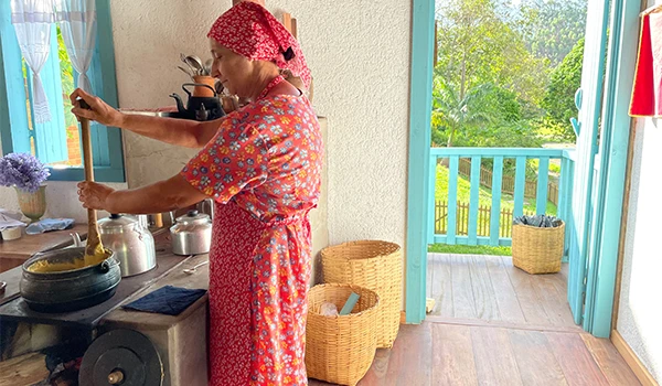 Mulher cozinhando Polenta o prato típico italiano, em uma cozinha com vista para a natureza, usando avental colorido. Na Rota das Montanhas Capixabas.
