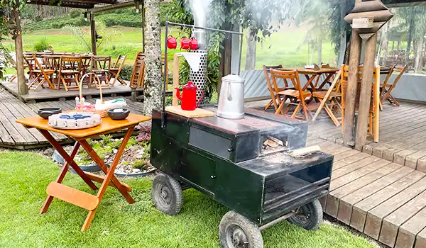 Carrinho de fazer Polenta com fumaça saindo, uma mesa de refeições ao fundo em um ambiente ao ar livre. Na Rota das Montanhas Capixabas.