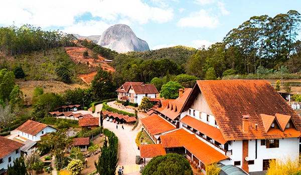 Vista aérea de uma linda cidade de Domingos Martins com chalés rústicos, cercada por belos jardins, no pé de uma montanha imponente e verdejante. Rota das Montanhas Capixabas.