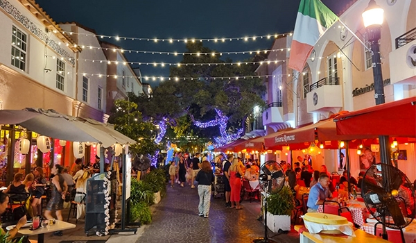 Rua animada à noite com refeições ao ar livre, decoração festiva e pessoas socializando sob luzes. Ideal para jantar em ambientes vibrantes.