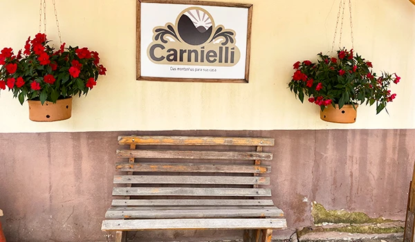 Imagem da Fazenda  Carnielli, mostrando a placa com o nome da marca e um banco de madeira decorado com flores vermelhas. Um dos lugares para fazer degustação de café Rota das Montanhas Capixabas.