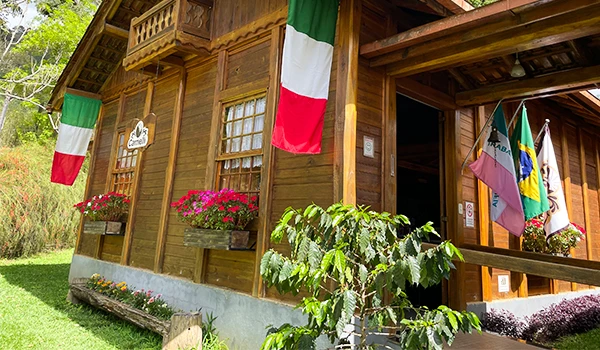 Imagem de uma típica casa italiana decorada com bandeiras do Brasil e da Itália, apresentando flores na fachada. Fazenda Carnielli na  Rota das Montanhas Capixabas.