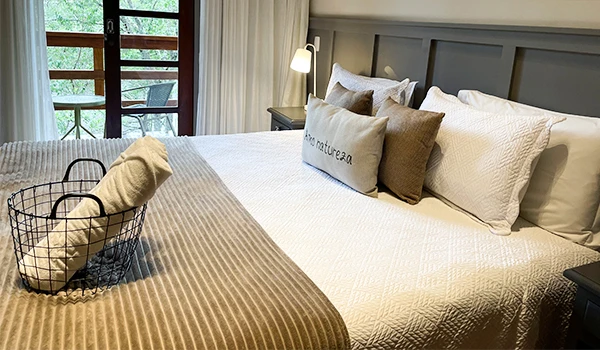 Uma cama confortável decorada com almofadas e cobertor em um quarto bem iluminado, foto do quarto do Hotel Natureza Eco Lodge, na Rota das Montanhas Capixabas.