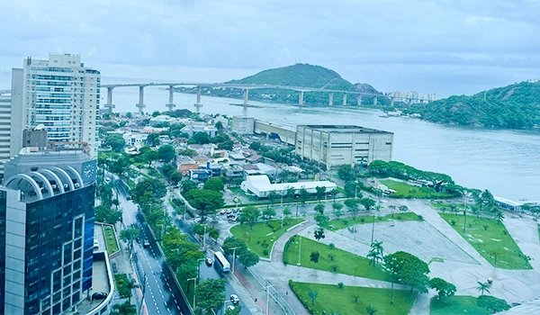 Vista panorâmica da cidade de Vitória com destaque para a ponte e a orla em um dia nublado. A imagem captura a harmonia entre a infraestrutura urbana e a natureza.