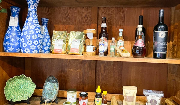 Prateleira de madeira com diversos produtos, incluindo garrafas, pacotes de chá e itens decorativos. Um charme para qualquer ambiente.