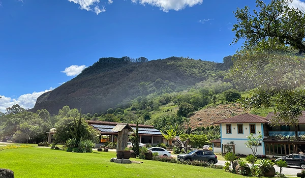 Vista panorâmica de uma área verde com montanhas ao fundo, destacando uma construção em estilo rústico e vegetação abundante. Cena da Rota das Montanhas Capixabas.