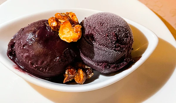Delicioso sorvete de açaí servido em uma taça, com uma camada de castanhas crocantes por cima. Uma sobremesa refrescante e nutritiva.