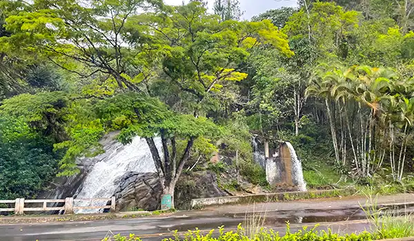 Vista deslumbrante da natureza com uma cachoeira cercada por árvores verdes e uma estrada tranquila, ideal para quem busca paz e beleza natural. Faz parte da Rota das Montanhas Capixabas.