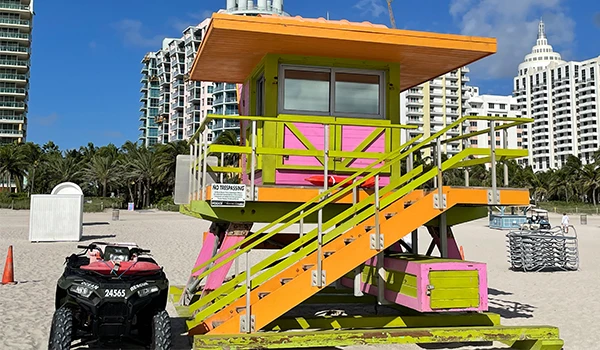 Praia em Miami com um colorido salva-vidas em estilo vibrante, rodeado por prédios modernos e vegetação tropical.