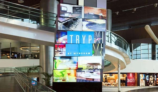 Imagem do interior do hotel TRYP by Wyndham, destacando um grande painel de LED com diversas imagens coloridas e ambientes modernos.