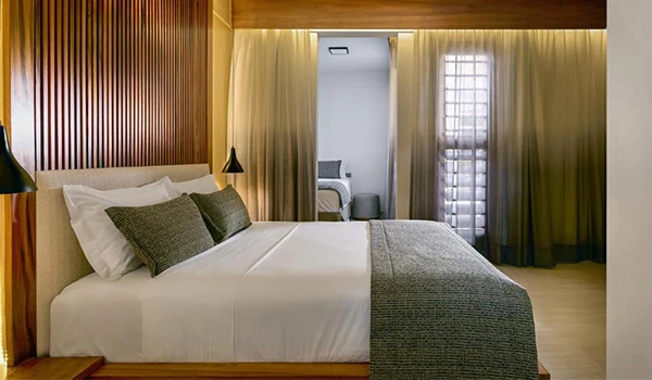 Quarto moderno e aconchegante com decoração em tons neutros, cama de casal com lençóis brancos e almofadas, iluminação suave e janelas com cortinas.