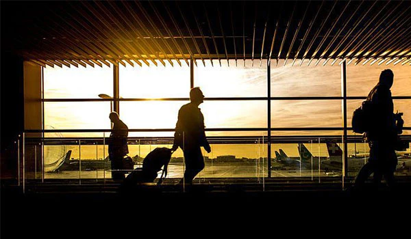 Silhuetas de pessoas caminhando em um aeroporto durante o pôr do sol, com aviações ao fundo, criando uma cena de viagem e aventura.