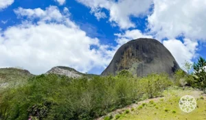 Vista deslumbrante do Pico da Bandeira, uma imponente formação rochosa cercada por vegetação exuberante e um céu azul claro.